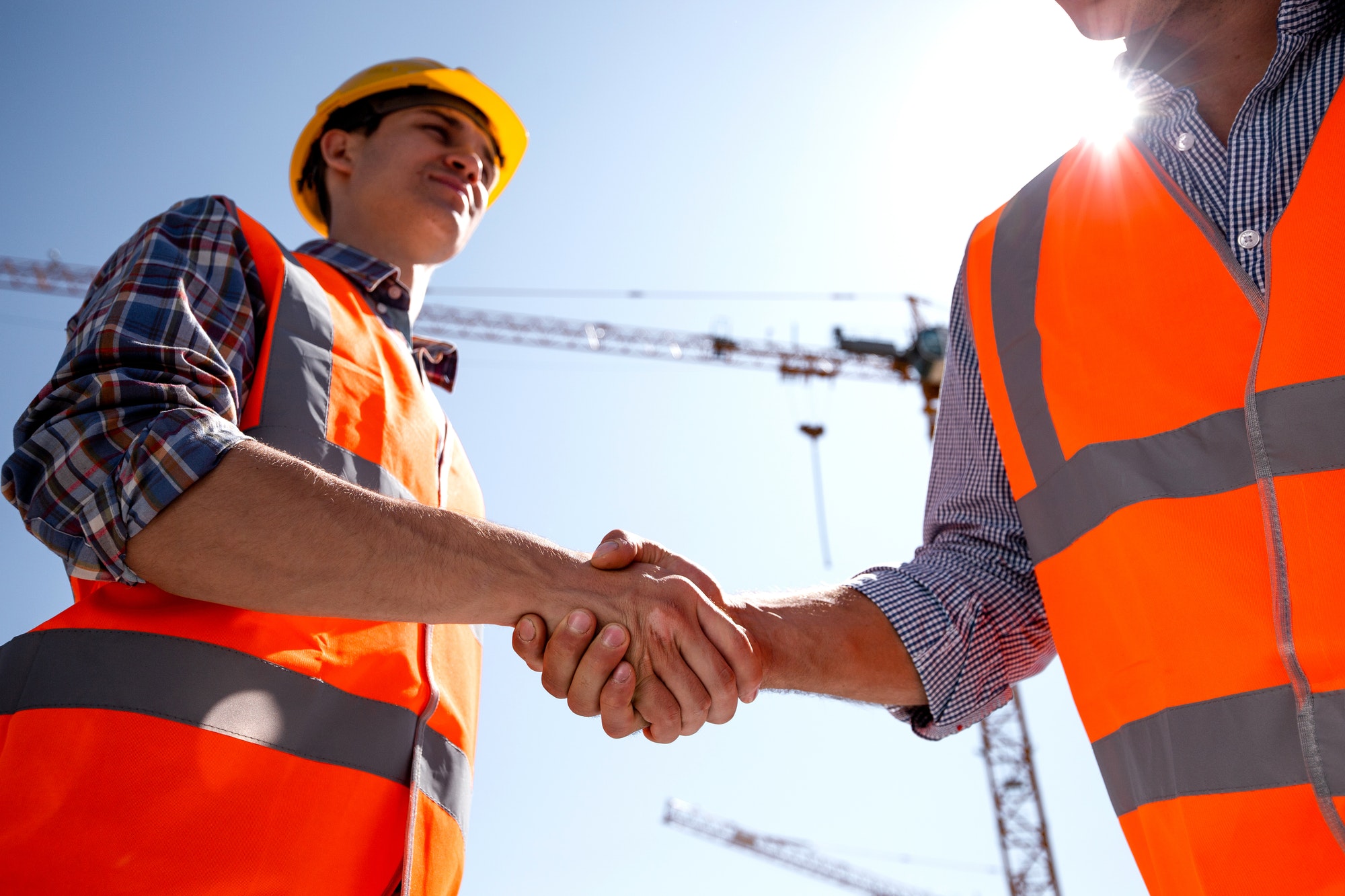 structural engineer and architect dressed in orange work vests and helmets shake hands on the